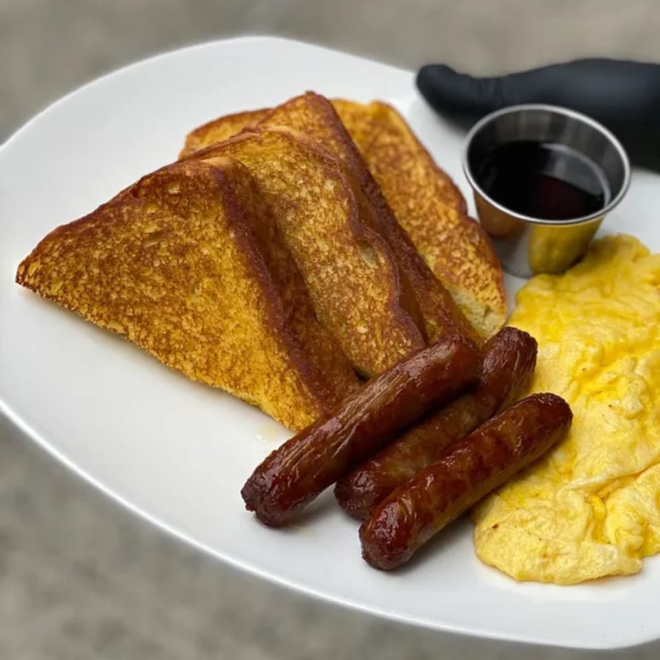 A Squire's Diner breakfast plate with French toast, sausage links, scrambled eggs, and syrup.
