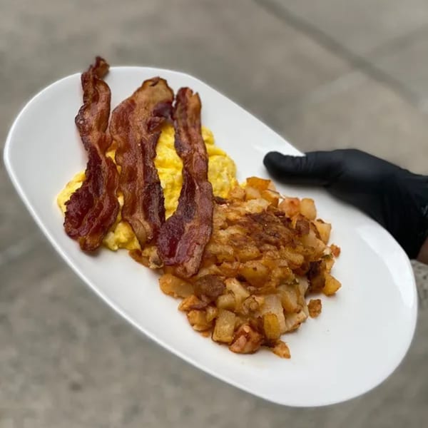 A white plate of scrambled eggs, crispy bacon, and golden hash browns from Squire's Diner.