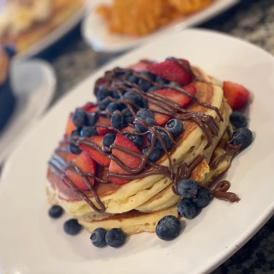 Stack of pancakes topped with strawberries, blueberries, and chocolate drizzle at Squire's Diner.