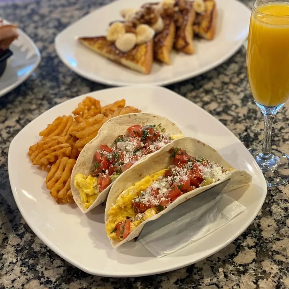 Breakfast tacos with scrambled eggs, pico de gallo, and cheese, served with waffle fries and orange juice.