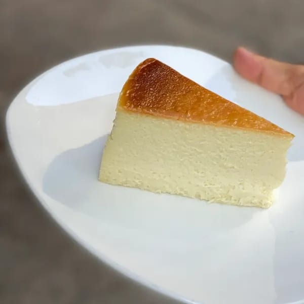 A slice of Squire's Diner cheesecake with a golden-brown top sits on a white plate.