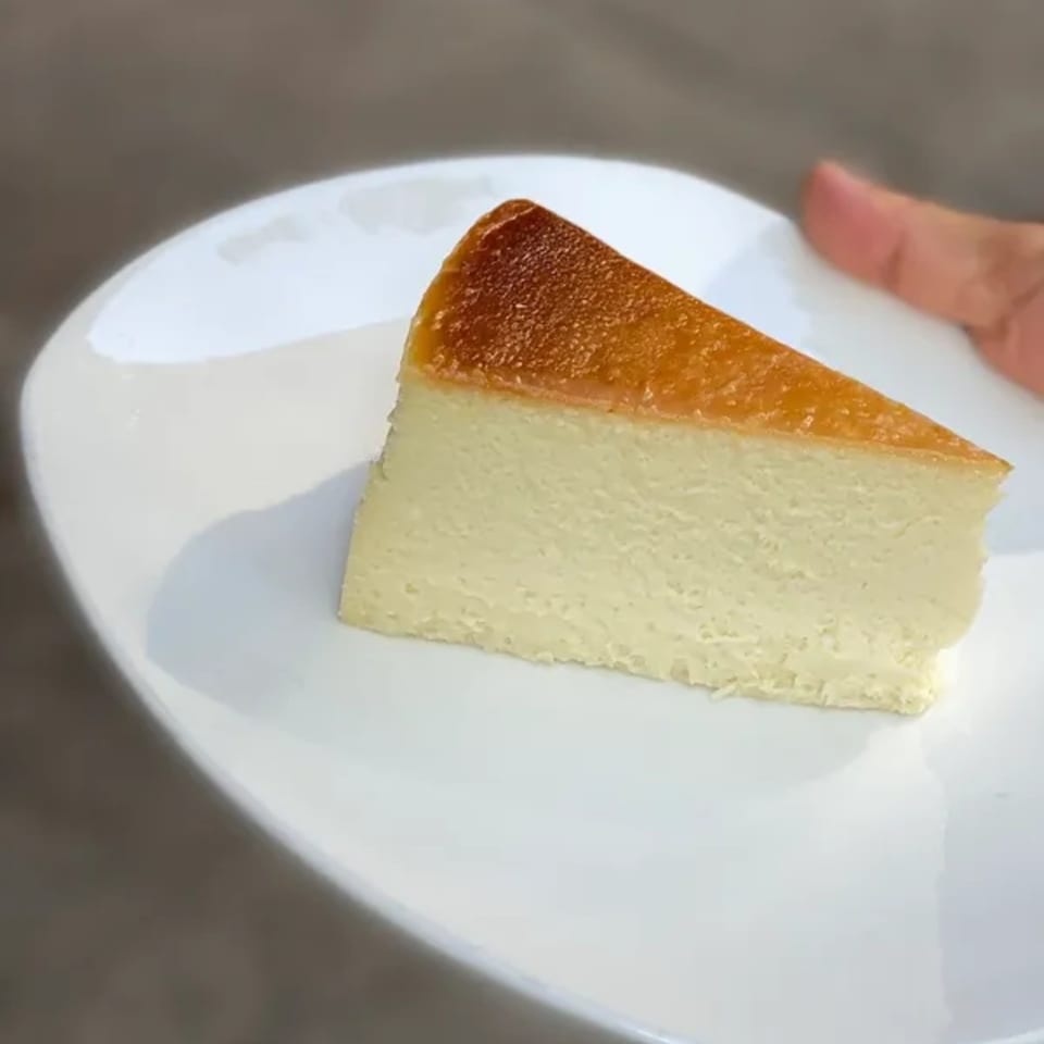 A slice of Squire's Diner cheesecake with a golden-brown top sits on a white plate.